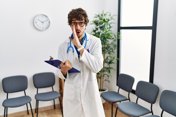 Fototapeta premium Young hispanic doctor man at waiting room hand on mouth telling secret rumor, whispering malicious talk conversation