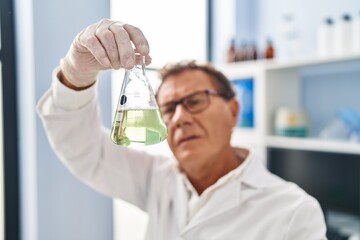 Middle age man wearing scientist uniform looking test tube at laboratory