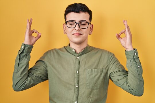 Non binary person standing over yellow background relax and smiling with eyes closed doing meditation gesture with fingers. yoga concept.
