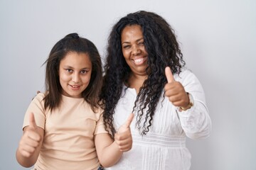 Mother and young daughter standing over white background approving doing positive gesture with hand, thumbs up smiling and happy for success. winner gesture.