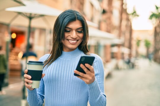 Young hispanic woman using smartphone and drinking a cup of coffee at the town - Powered by Adobe