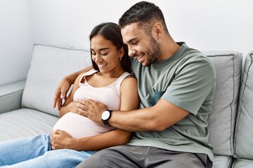 Latin man and woman couple hugging each other expecting baby at home