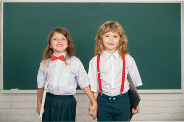 Cute little school kids friends studying together in classroom. Friendship in school, classmate concept. Cute school friends holding hand near blackboard.