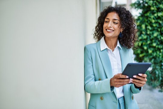 Young hispanic business woman wearing professional look smiling confident at the city using touchpad device