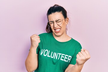 Young hispanic woman wearing volunteer t shirt very happy and excited doing winner gesture with arms raised, smiling and screaming for success. celebration concept.