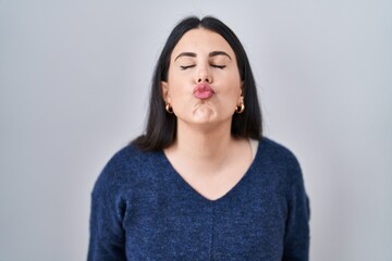 Young brunette woman standing over isolated background looking at the camera blowing a kiss on air being lovely and sexy. love expression.