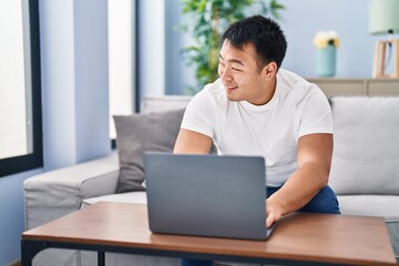 Fototapeta premium Young chinese man using laptop sitting on sofa at home