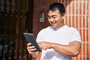 Young chinese man smiling confident using touchpad at street