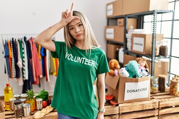 Asian young woman wearing volunteer t shirt at donations stand making fun of people with fingers on forehead doing loser gesture mocking and insulting.