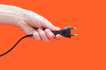 Electric plug for a socket in a hand on an orange background. The concept of electricity and its...