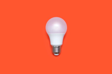 An energy-saving light bulb on an orange background in the center of the image. Saving energy and finances. Electrical equipment and the evolution of light. Disposable light bulb
