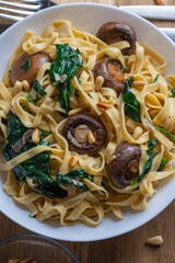 Rustic pasta with mushrooms, creamy spinach sauce and parsley on a wooden background