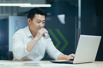 Successful Asian businessman working in modern office, man drinking purified water and smiling