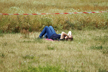Naklejka na ściany i meble A desperate young woman lies on a meadow in a park in Berlin-Germany on a warm and sunny day and holds her hands to her head