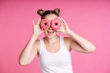 Caucasian teenage girl covering eyes with pink doughnuts
