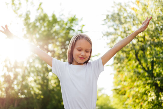 Smiling girl standing with raised hands at sunset outdoor. Happy child having fun. Mental health, freedom concept