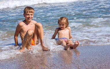 Two happy children a boy and a girl are sitting on the seashore in the waves and laughing, happy childhood holidays, traveling with children