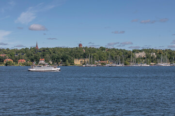 Fototapeta na wymiar Old harbor ferry passing the island Djurgården a sunny summer day in Stockholm