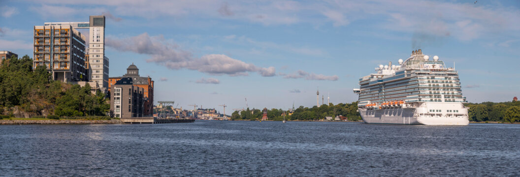 Large cruise ship passing the pier and island Kvarnholmen with water front apartment houses in the morning a sunny summer day in Stockholm