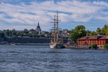 Fototapeta na wymiar New old style sail ship at a pier and the ridge of the district Södermalm a sunny summer day in Stockholm