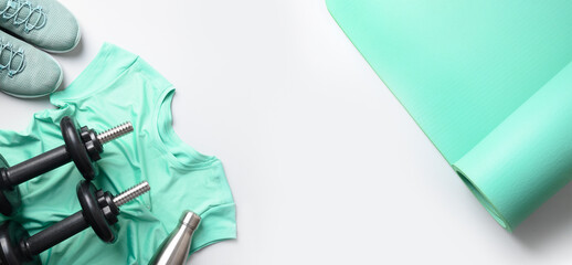 Sport and fitness equipment, female tee-shirt, yoga mat, shoes, water bottle on gray background. Banner with copy space. View from above.