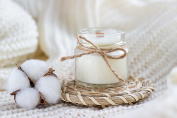 Fototapeta na wymiar Soy wax candle with cotton flower on white cozy blanket