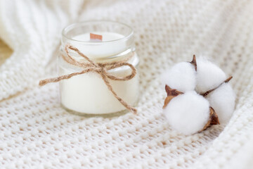 Soy wax candle with cotton flower on white cozy blanket