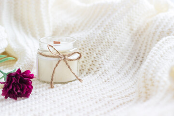 Fototapeta na wymiar Handmade candle with red flower on white cozy blanket