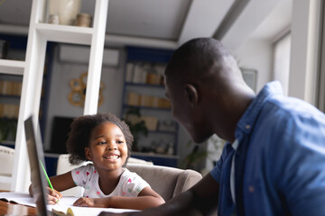 Image of happy african american father and daughter doing homework together