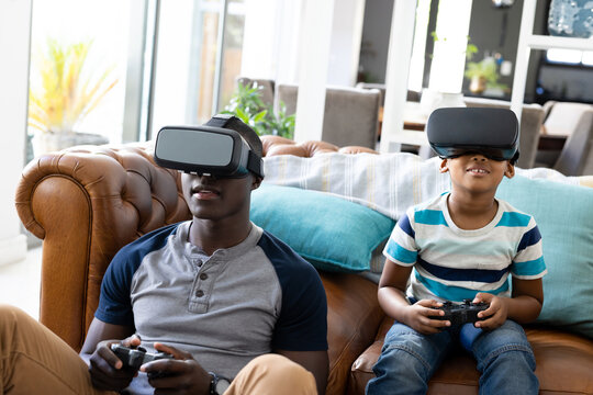 Image of african american father and son playing games on the console and using vr headset