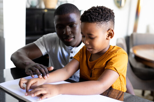 Image of african american father and son reading braille