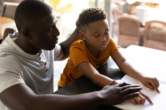 Image of african american father and son reading braille - Powered by Adobe