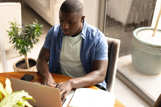 Image of hands of african american man with smartphone and laptop working from home