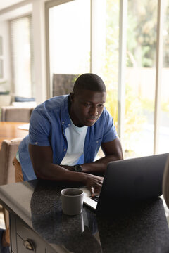 Vertical image of african american man drinking coffee and using laptop