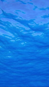 VERTICAL VIDEO: Underwater shot, surface of blue water with sun rays. Natural background with sun glints on surface of blue water. Texture of blue water surface 