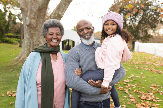 Image of happy african american grandparents and granddaughter in autumn garden