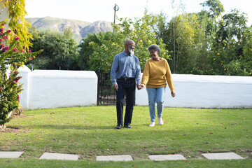 Image of happy african american senior couple walking in garden