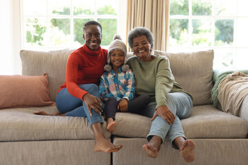 Image of happy african american three generation women sitting on sofa and having fun - Powered by Adobe