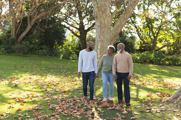 Image of happy african american parents and adult son walking in garden