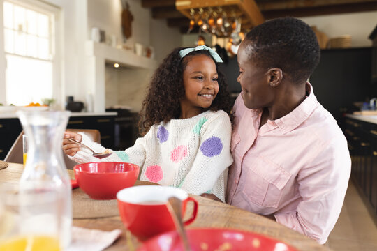 Image of happy african american girl eating breakfast with mother - Powered by Adobe