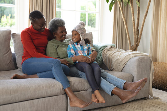 Image of happy african american three generation women sitting on sofa and having fun