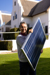 Vertical image of happy caucasian senior man with solar panel in garden