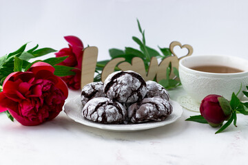 Treats on a white table. Chocolate cracks cookies, a cup of tea and peonies