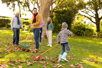 Image of happy caucasian multi generation family swiping leaves in autumn garden