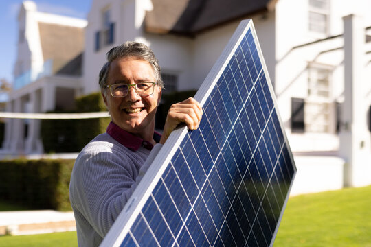 Vertical image of happy caucasian senior man with solar panel in garden