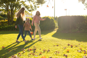 Image of three generation of caucasian women walking in autumn garden
