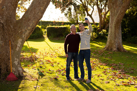 Image of happy caucasian father and adult son taking selfie in garden