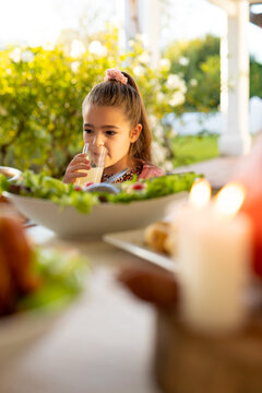 Vertical image of caucasian girl drinking juice during family dinner