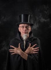 Portrait of a mysterious male magician in a black high top hat and black robe.