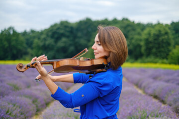 Close-up adult caucasian woman violinist playing violin on summer lavender field, romantic musician...